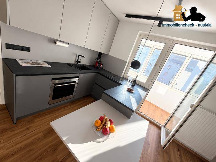 Moderne Küche mit grauen Schränken, integriertem Backofen und Zugang zu einem hellen Balkon.
