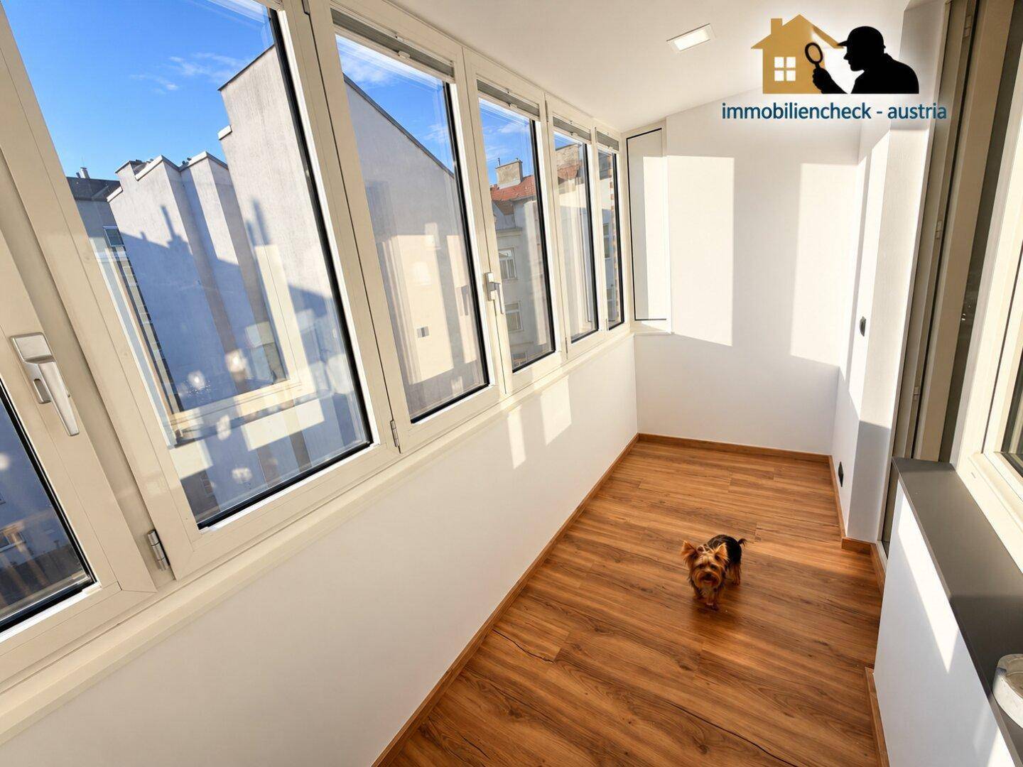 Sonniger, verglaster Balkon mit Laminatboden und weitem Blick über die Stadt.