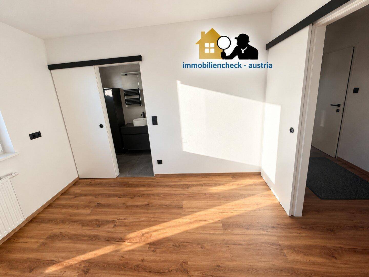Helles Schlafzimmer mit Laminatboden und modernen Schiebetüren zum angrenzenden Badezimmer.