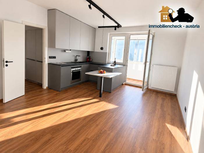 Geräumiger Wohnbereich mit integrierter Küche, Laminatboden und Zugang zu einem sonnigen Balkon.