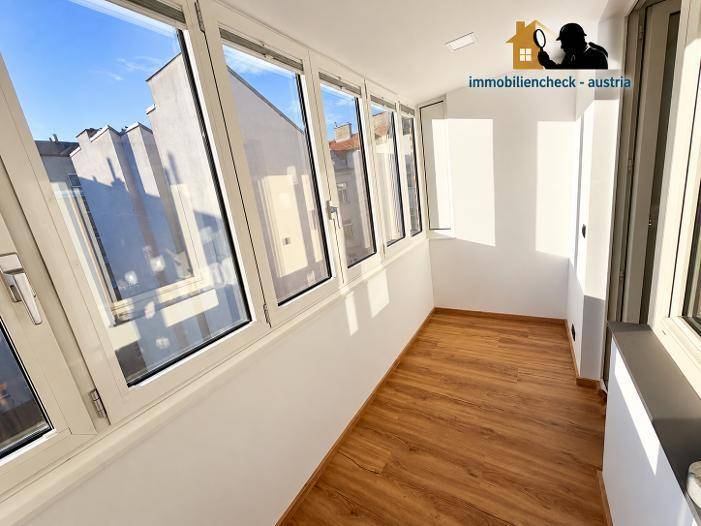 Heller, verglaster Balkon mit Laminatboden und Blick auf die umliegenden Gebäude.