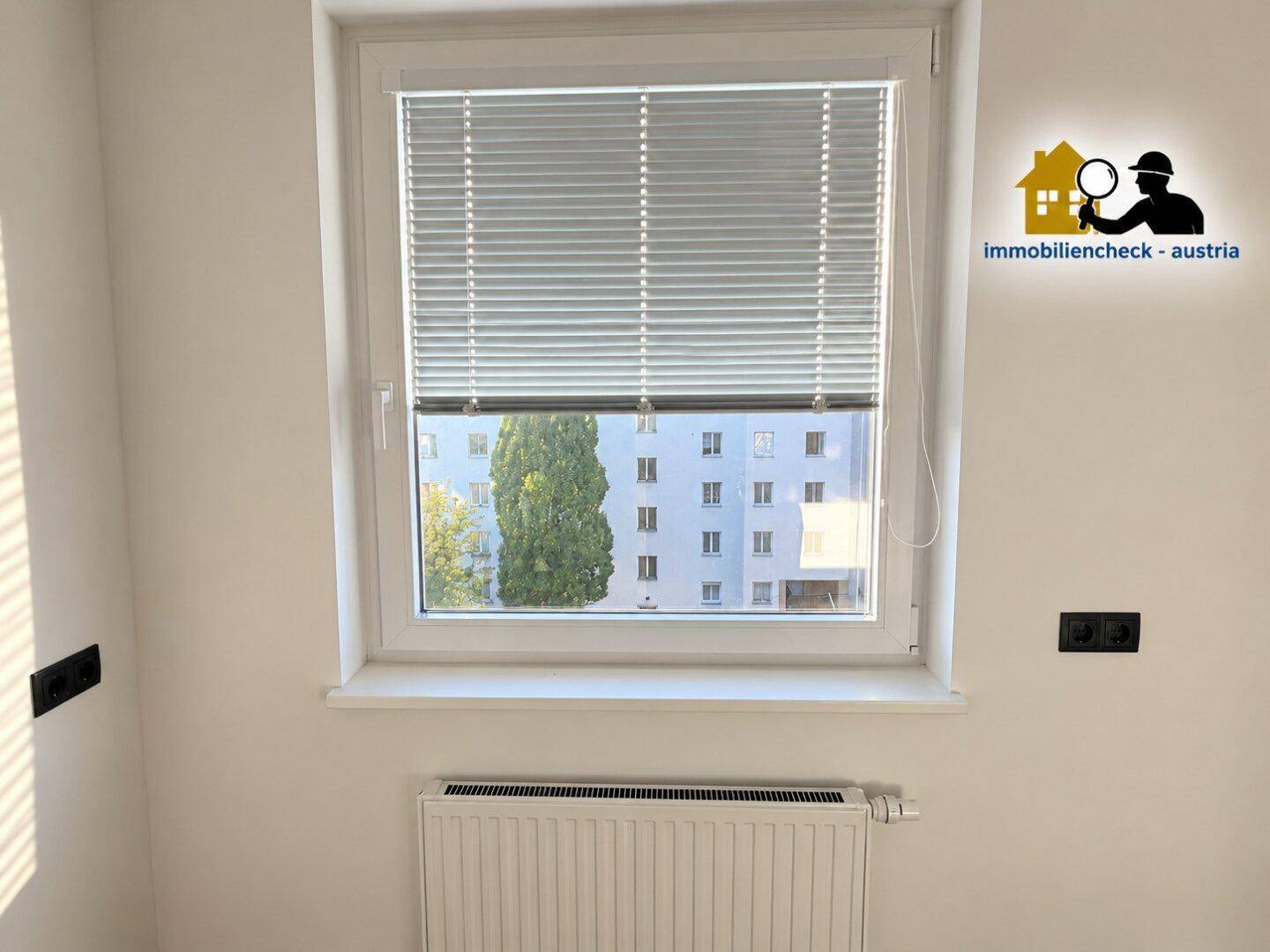 Fenster mit Jalousien und Blick auf ein gegenüberliegendes Gebäude.