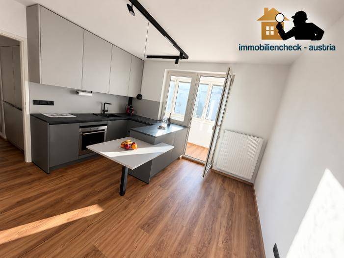 Heller Küchenbereich mit moderner Einbauküche, Laminatboden und Zugang zum verglasten Balkon.