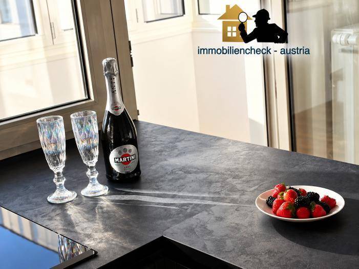 Moderne Küchenarbeitsplatte mit Sektflasche, Gläsern und frischen Beeren am Fenster.