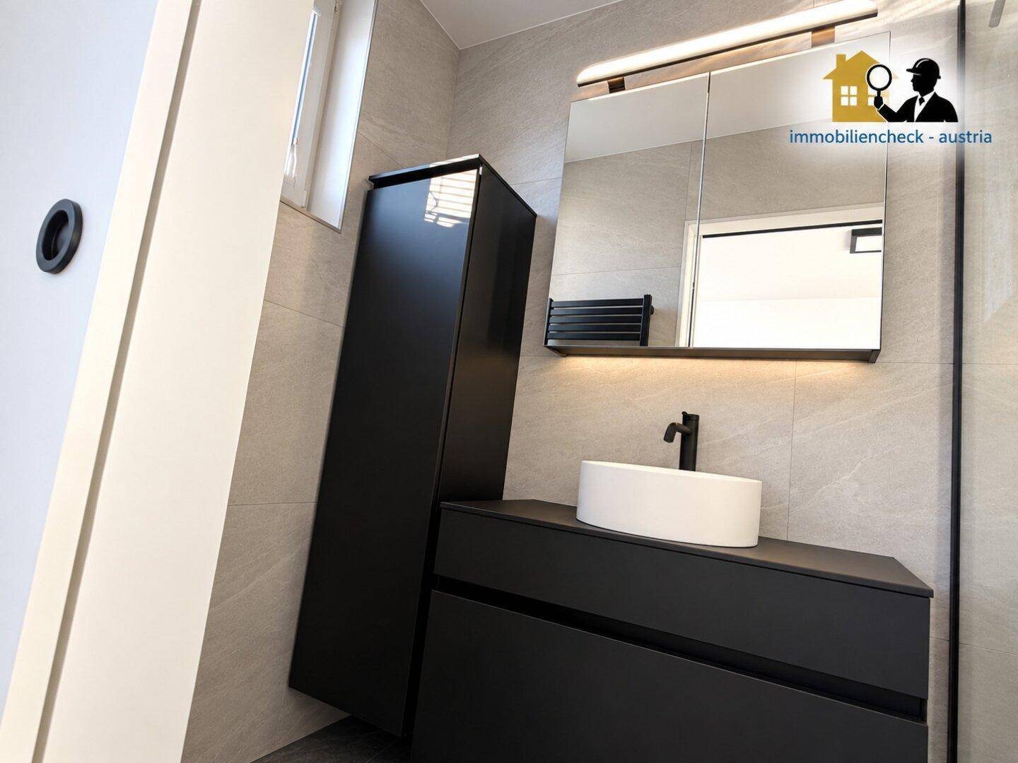 Modernes Badezimmer mit schwarzem Waschtisch, Aufsatzwaschbecken und beleuchtetem Spiegelschrank.