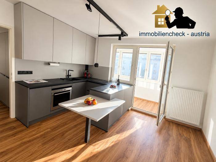 Moderne Küche mit grauen Schränken, dunkler Arbeitsplatte und integriertem Backofen, hell und funktional.
