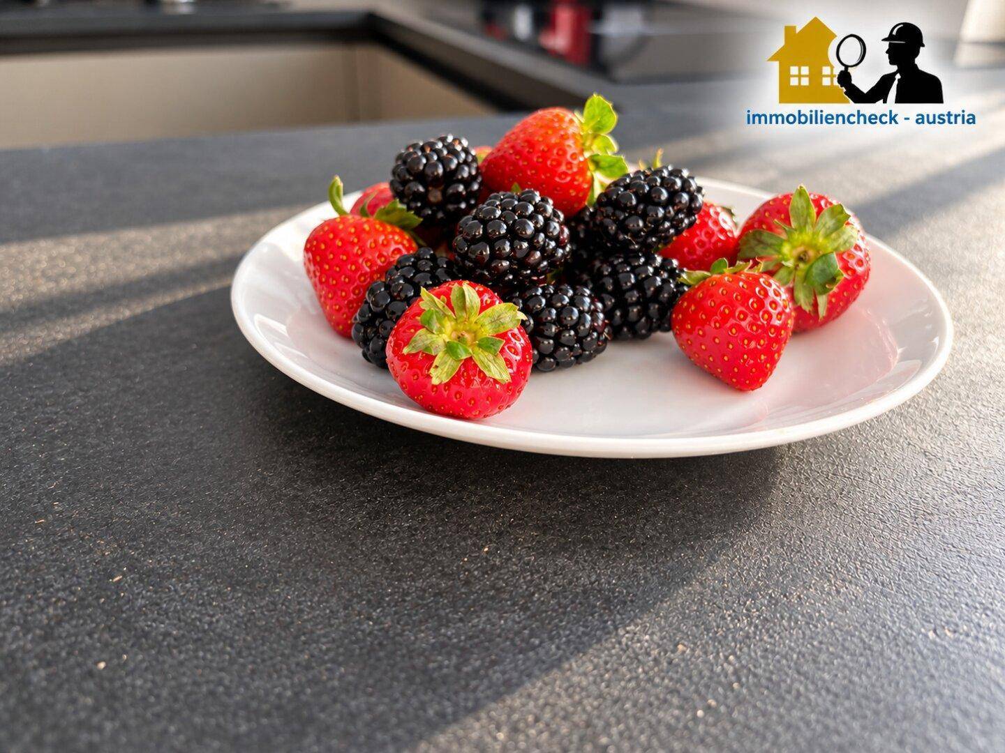 Nahaufnahme einer Platte mit frischen Erdbeeren und Brombeeren auf dunkler Küchenarbeitsplatte.