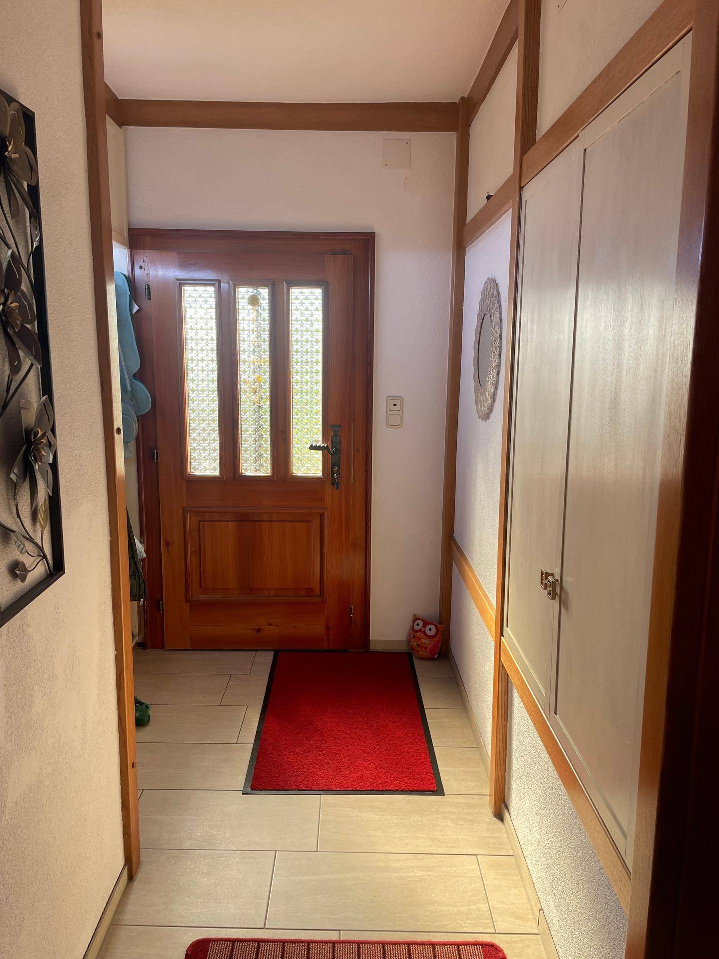 Heller Eingangsbereich mit Holztür, Fliesenboden und integrierten Schränken.