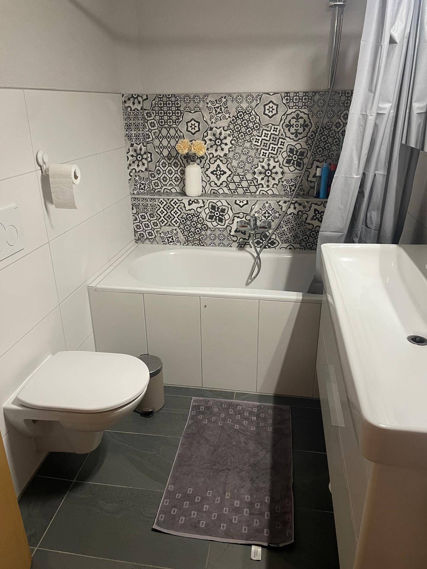 Modernes Badezimmer mit Badewanne, WC, Waschbecken und dekorativen Fliesen.
