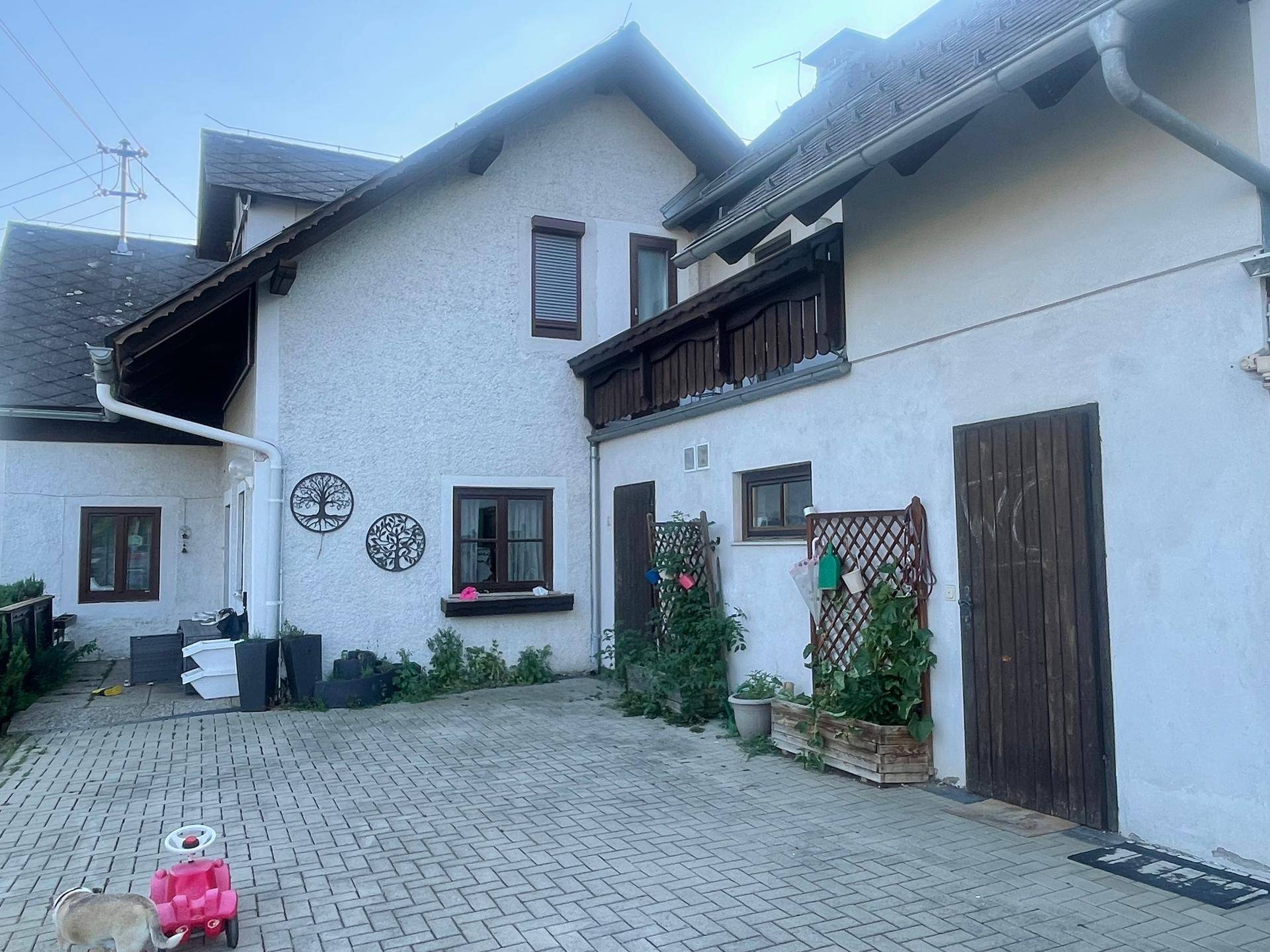 Rückseite des Hauses mit gepflastertem Hof, kleinem Balkon und Holztüren.