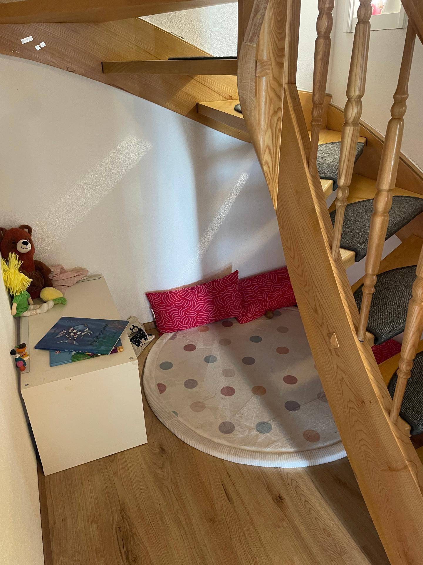 Gemütliche Leseecke unter der Holztreppe mit Teppich und Kinderspielzeug.