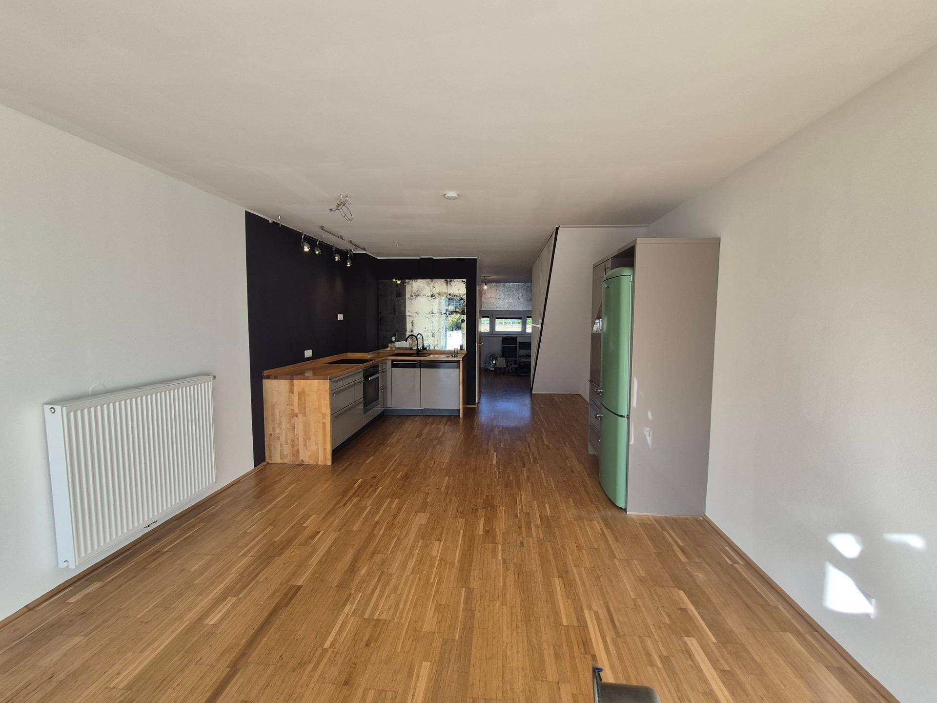 Heller offener Wohnbereich mit integrierter Küche, Holzboden und modernem Kühlschrank.