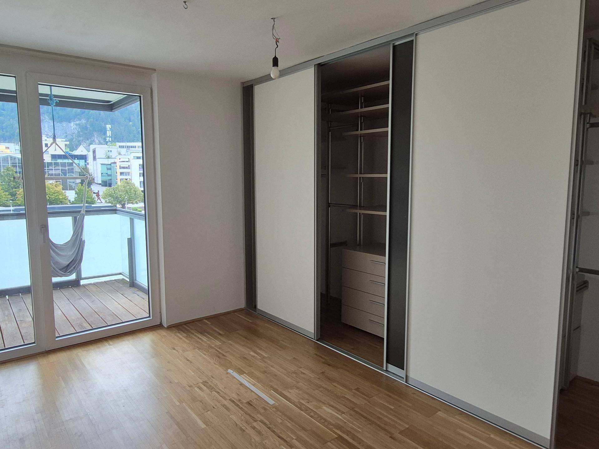 Schlafzimmer mit integrierten Schiebetürenschränken und Zugang zu einem Balkon mit Hängematte.