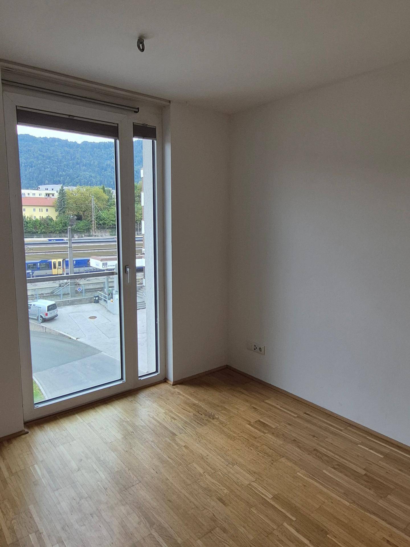 Helles Schlafzimmer mit Holzboden, großen Fenstern und Blick auf Berge und Bahngleise.