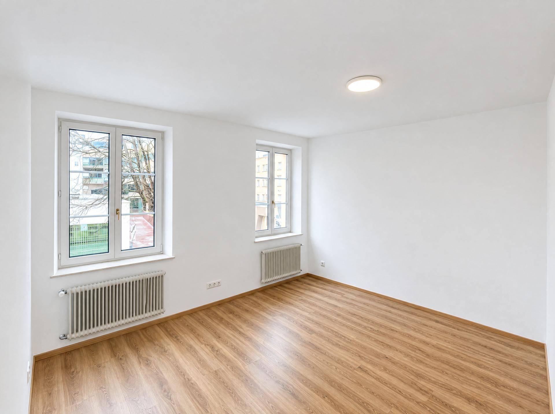 Heller, leerer Raum mit Laminatboden und zwei Fenstern, ideal als Wohnzimmer nutzbar.