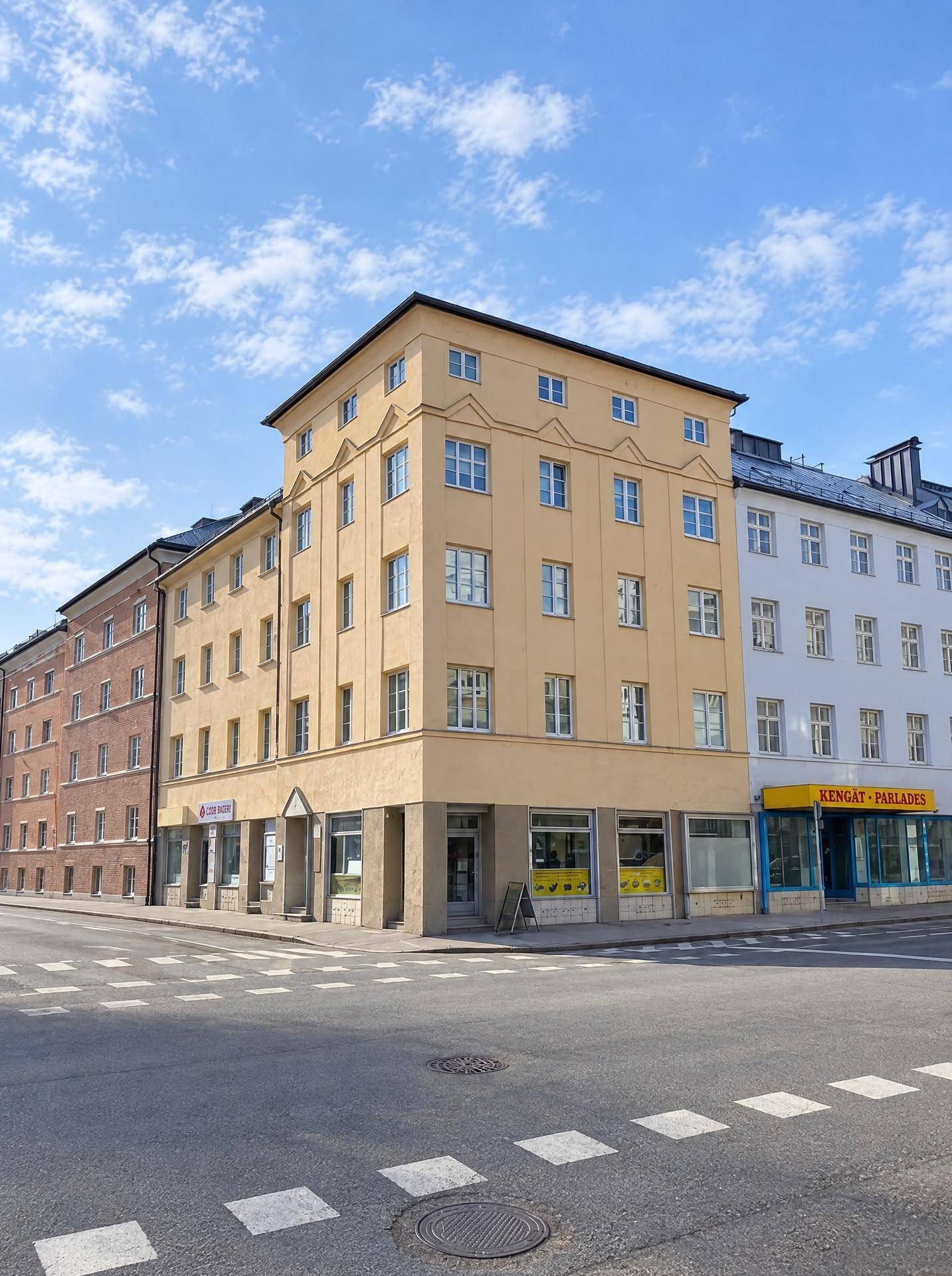 Eine weitere Ansicht des gelben Eckgebäudes mit seinen vielen Fenstern und der belebten Straßenkreuzung.
