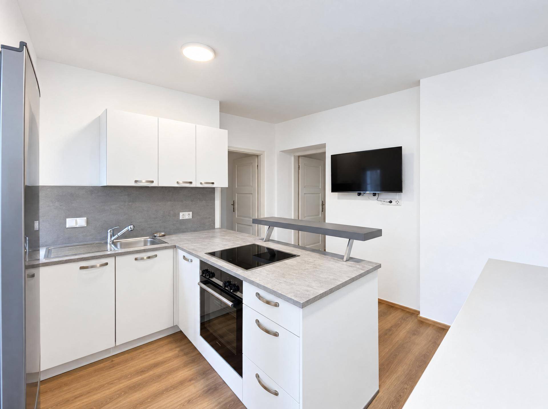 Moderne Küche mit weißen Schränken, Induktionskochfeld, Backofen und Wandfernseher.
