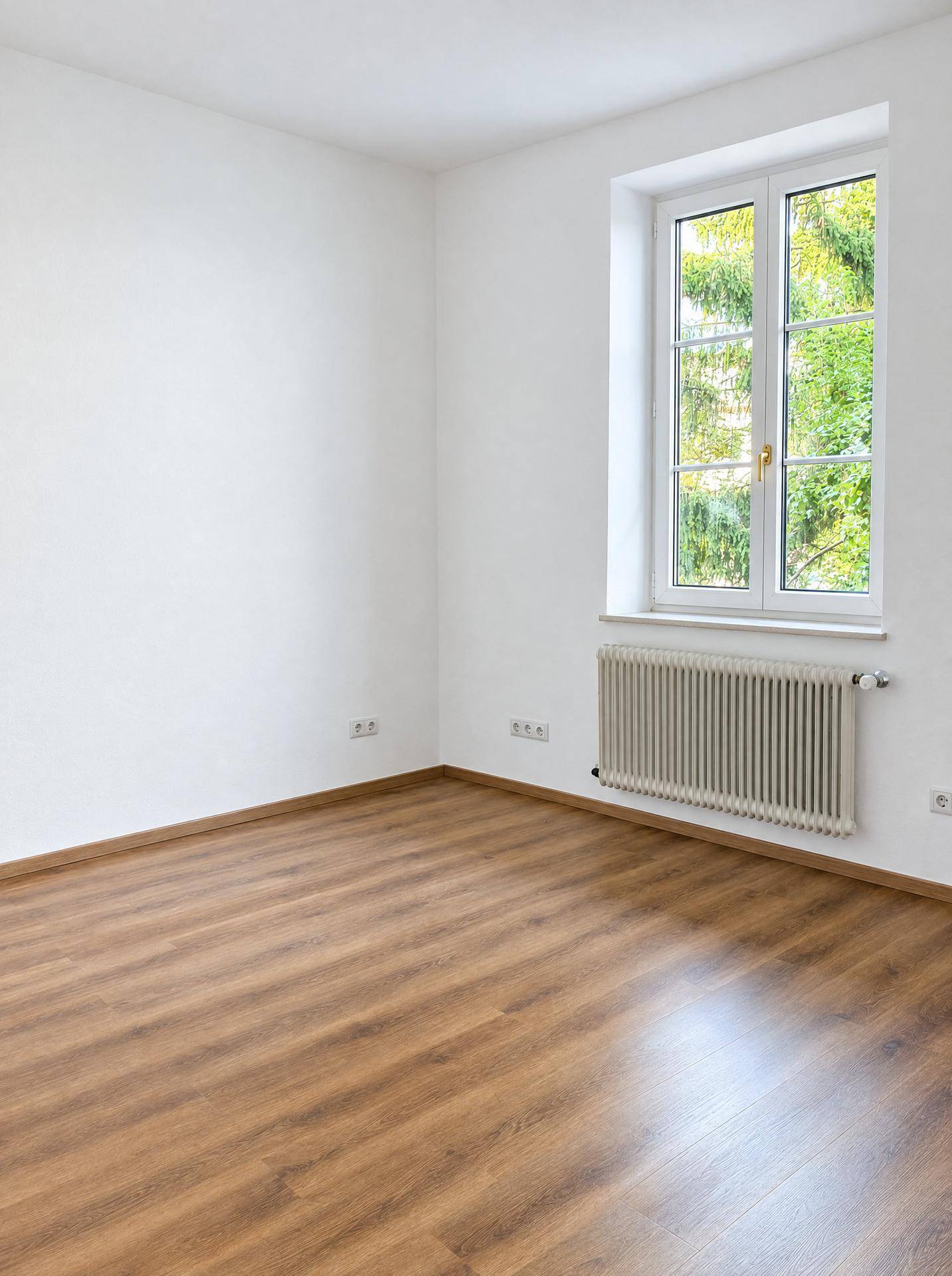 Heller, leerer Raum mit Laminatboden und Fenster mit Blick ins Grüne, ideal als Schlafzimmer.