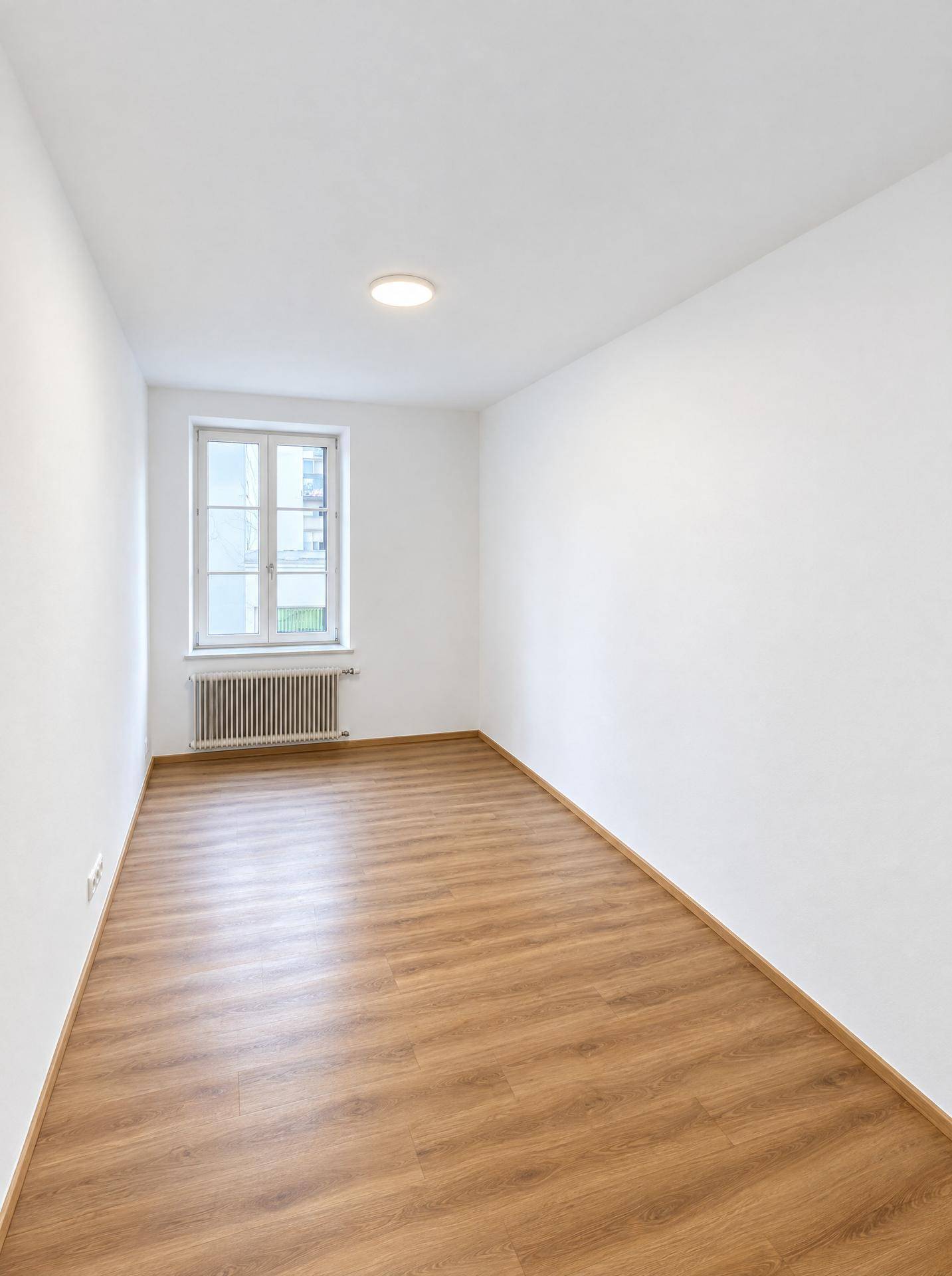 Leerer, heller Raum mit Laminatboden und einem Fenster, gut geeignet als Kinder- oder Gästezimmer.