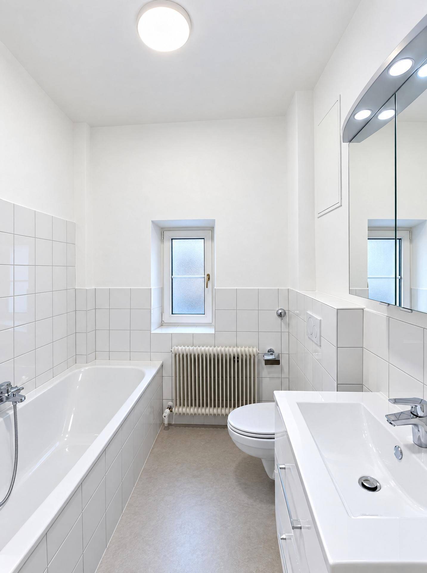 Helles Badezimmer mit Badewanne, WC, Waschbecken und Spiegelschrank, weiß gefliest.