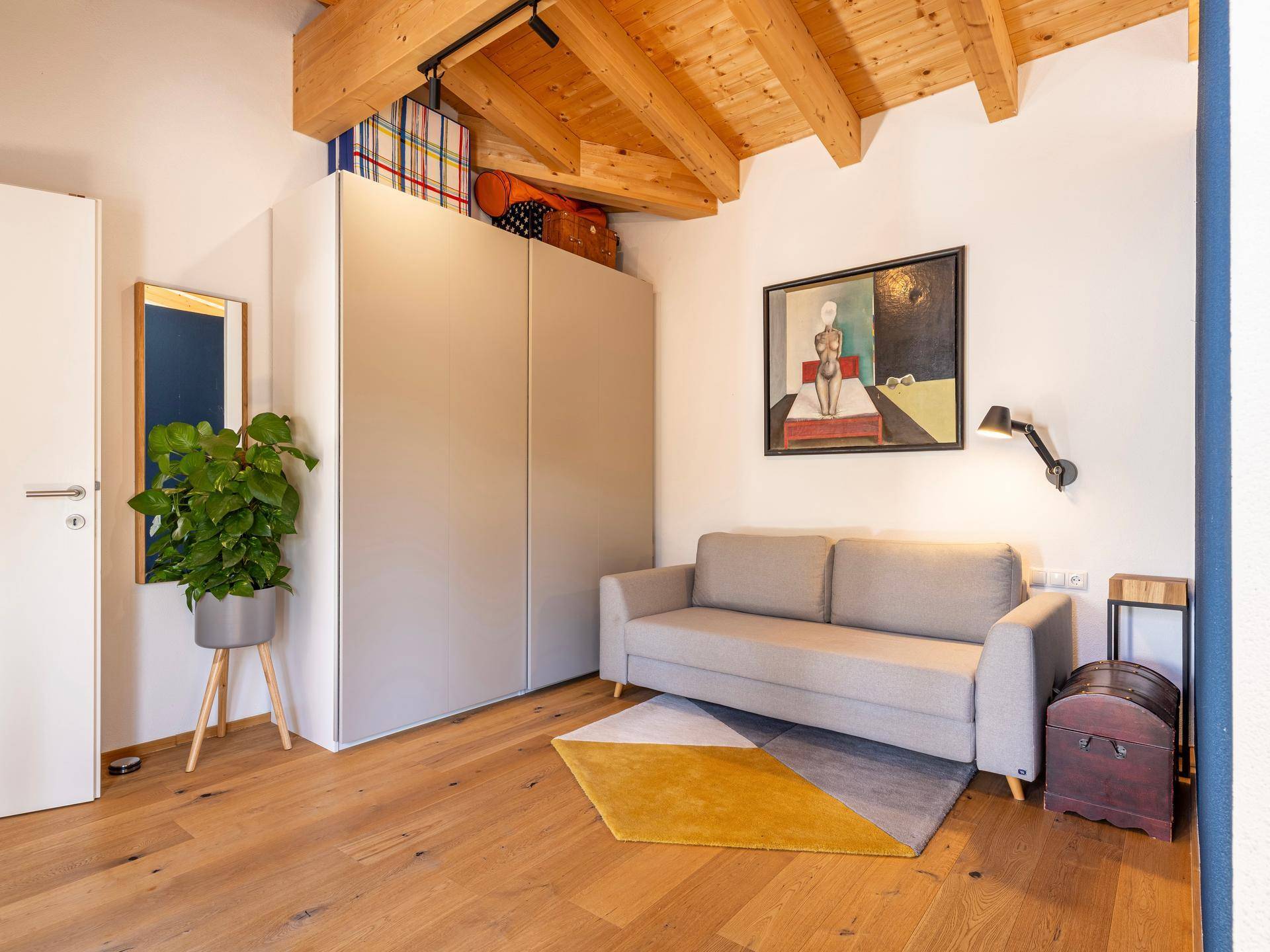 Gemütliches Zimmer mit Sofa, Kleiderschrank und sichtbaren Holzbalken an der Decke.