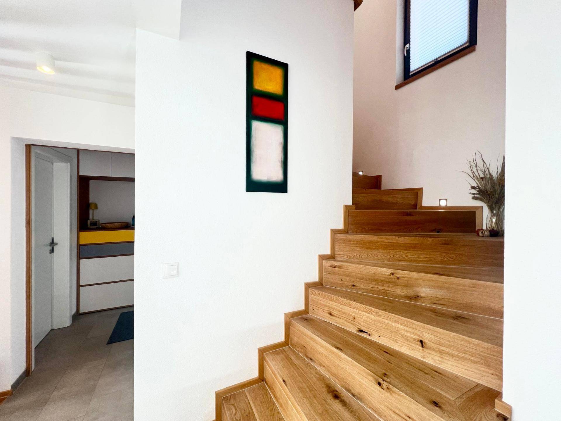 Elegante Holztreppe in einem hellen Flur mit modernem Kunstwerk.