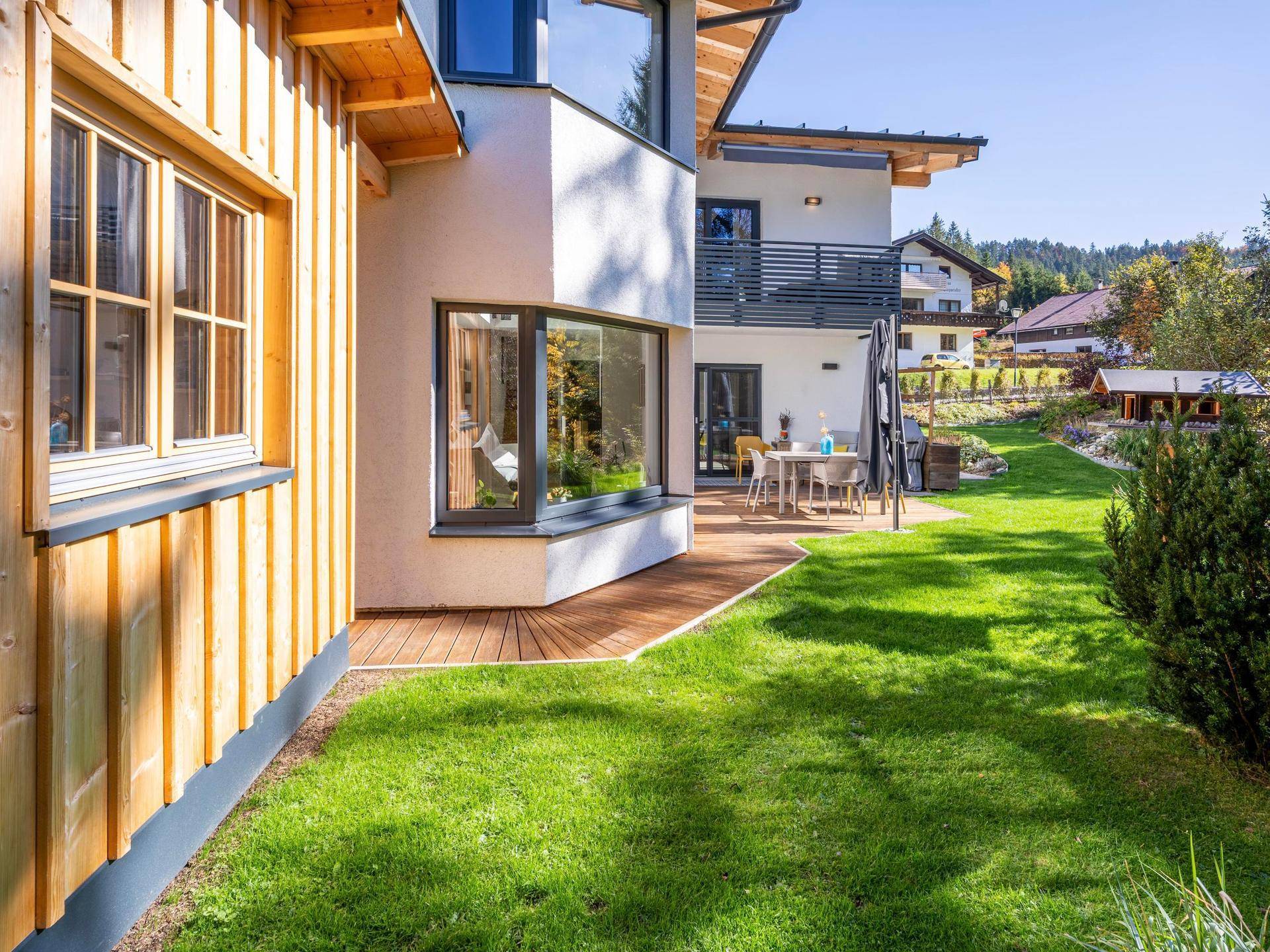 Seitlicher Blick auf das Haus mit Holzfassade, Rasenfläche und einer Holzterrasse.