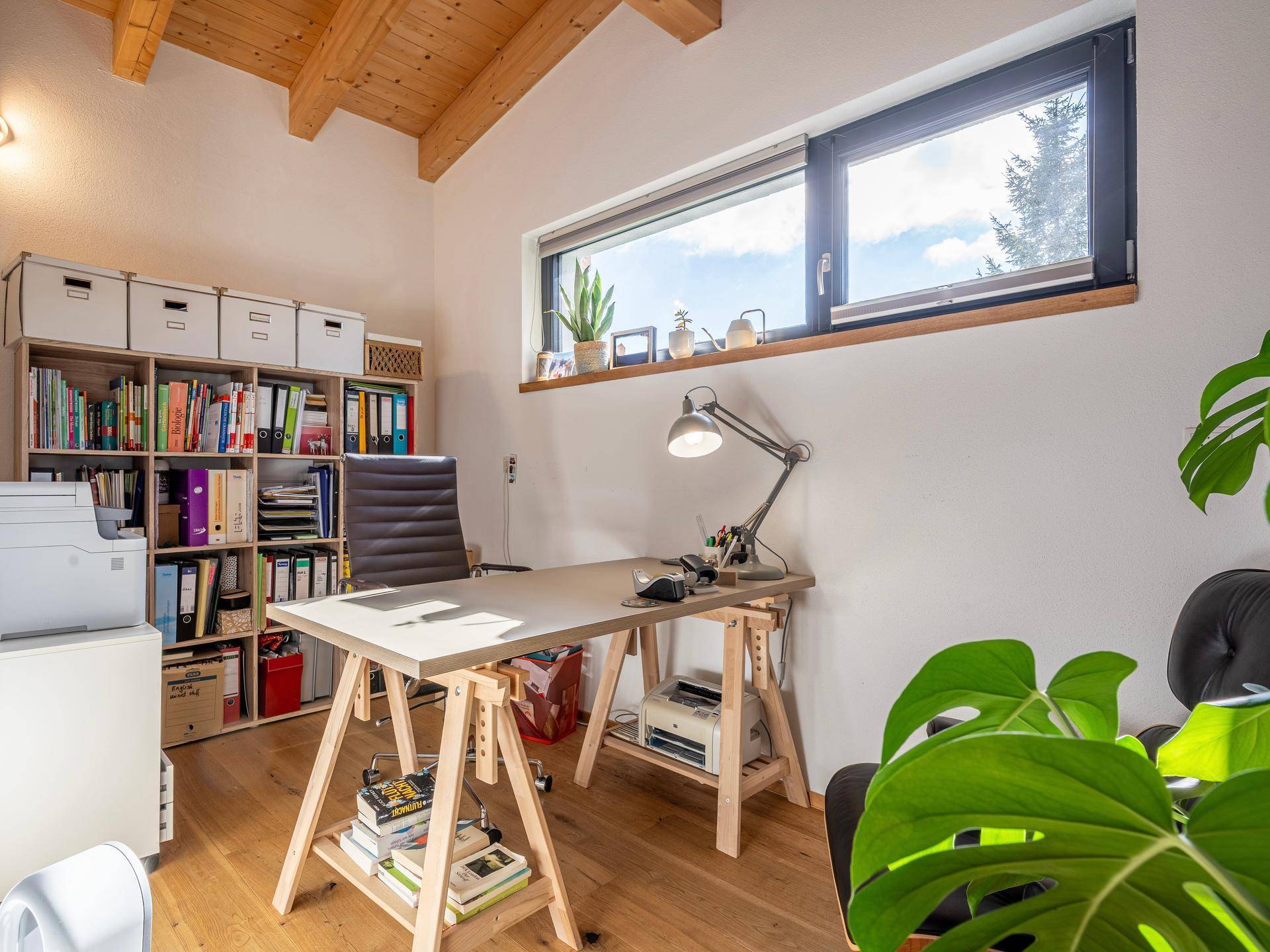Helles Arbeitszimmer mit Holzboden, Bücherregalen und großem Fenster.
