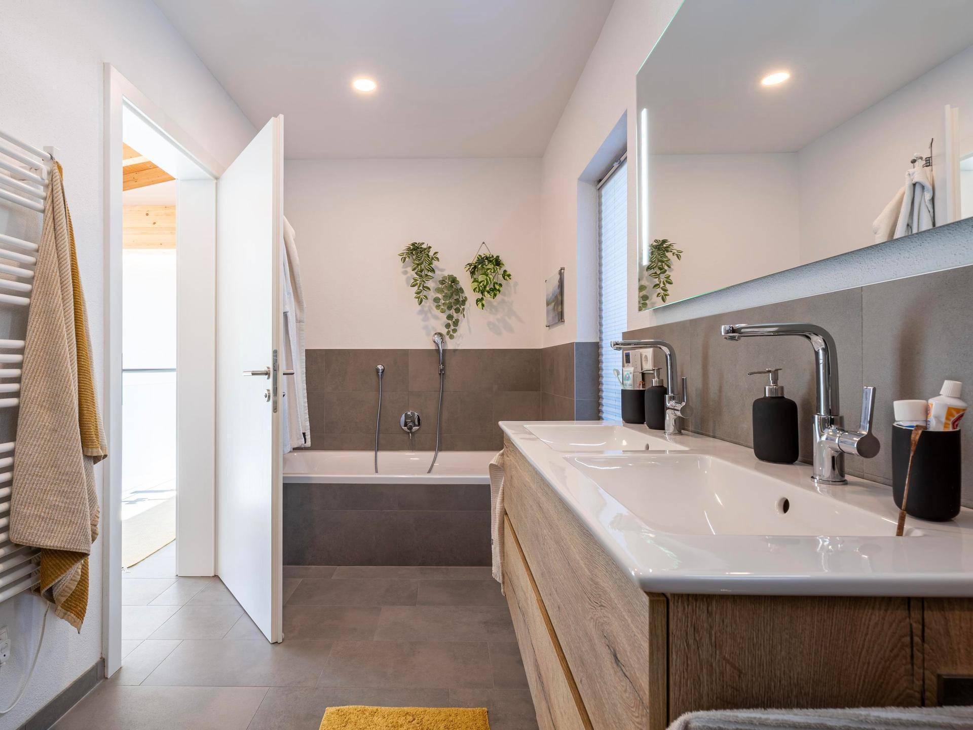 Modernes Badezimmer mit Doppelwaschbecken, Badewanne und grauen Fliesen.