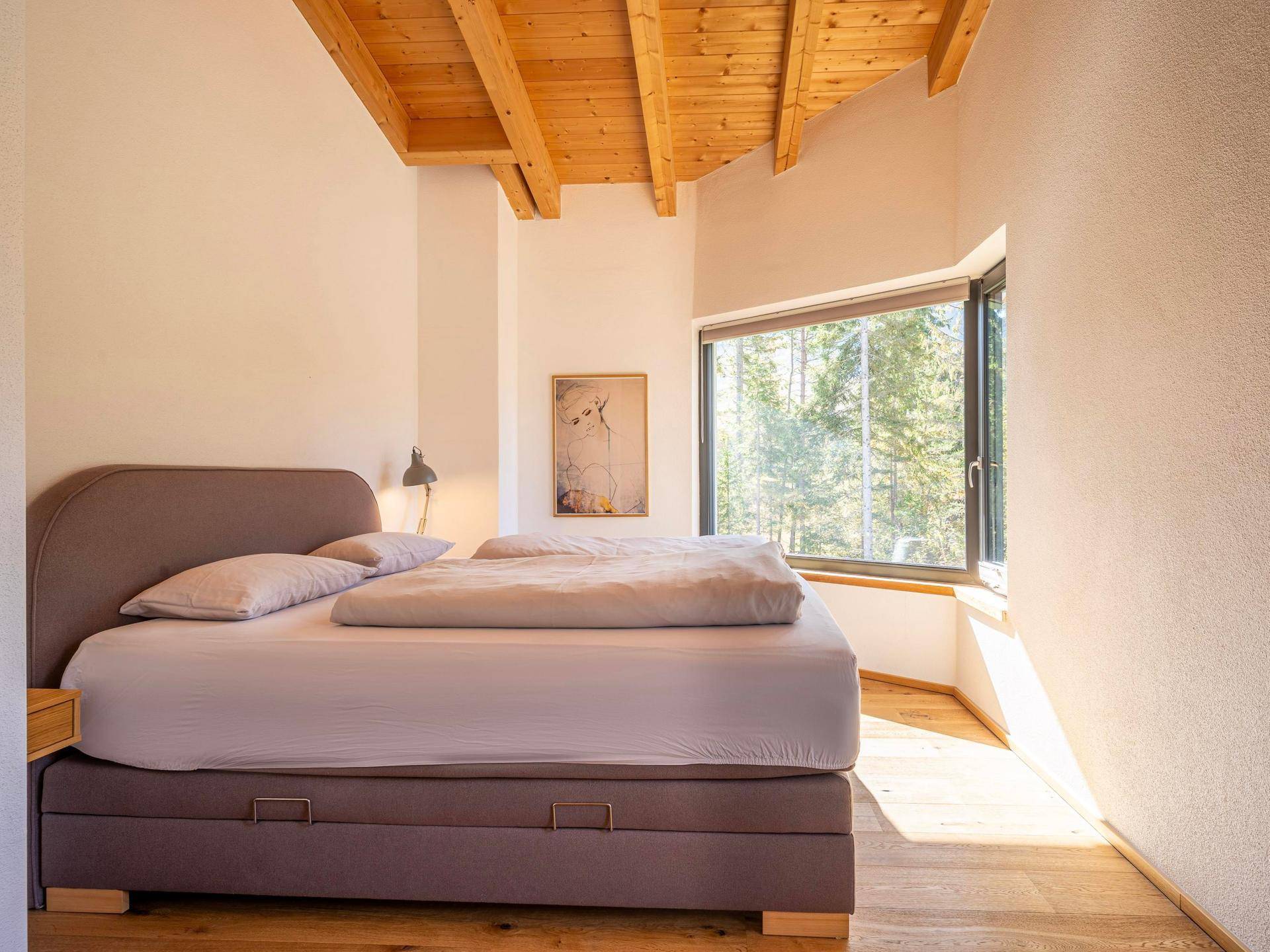 Gemütliches Schlafzimmer mit Holzboden, sichtbaren Holzbalken und Waldblick.