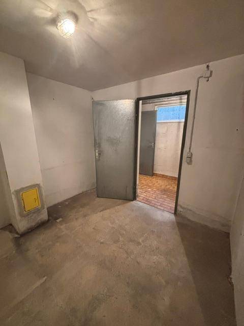 Leerer Kellerraum mit Betonboden und robuster Metalltür.