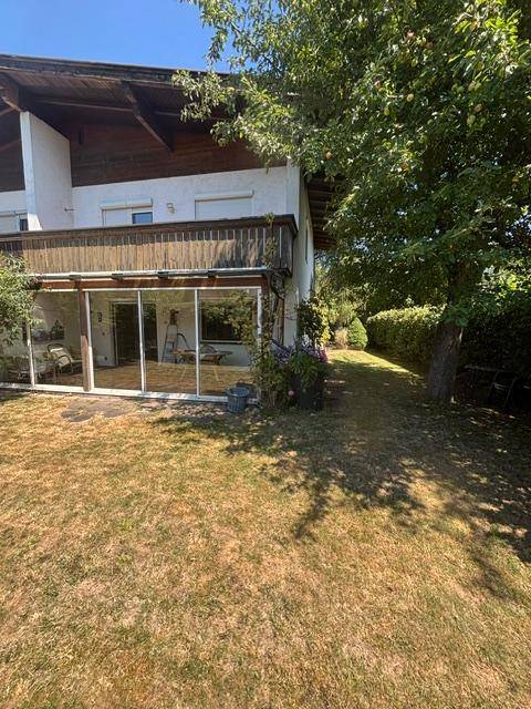 Rückansicht des Hauses mit Wintergarten und trockenem Rasenbereich im Sommer.