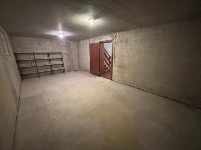 Geräumiger Kellerraum mit Betonwänden, Regalen und Zugang zu einer Treppe.