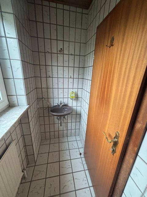 Gäste-WC mit kleinem Waschbecken, Fliesenwänden und Fenster für Tageslicht.