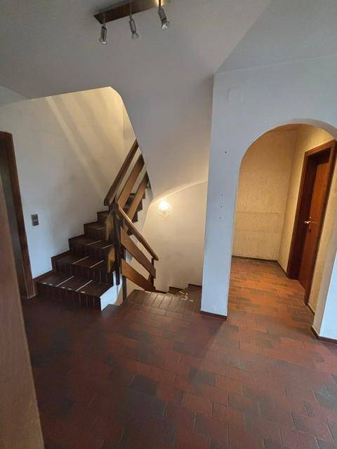 Heller Flur mit Holztreppe, Terrakotta-Fliesenboden und einem Rundbogen.