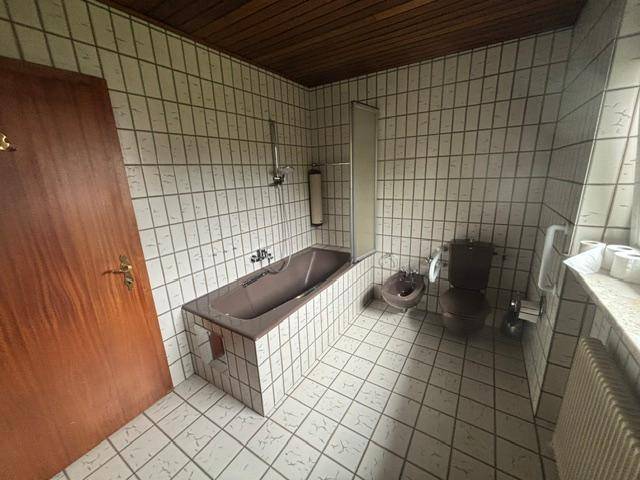 Badezimmer mit Badewanne, Bidet, WC und Fliesen im Stil der 80er Jahre.