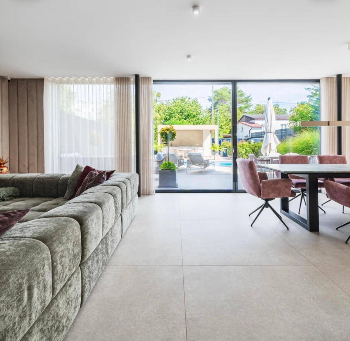 Heller Wohn- und Essbereich mit großen Glasfronten, die den Blick auf den Garten und den Pool freigeben.