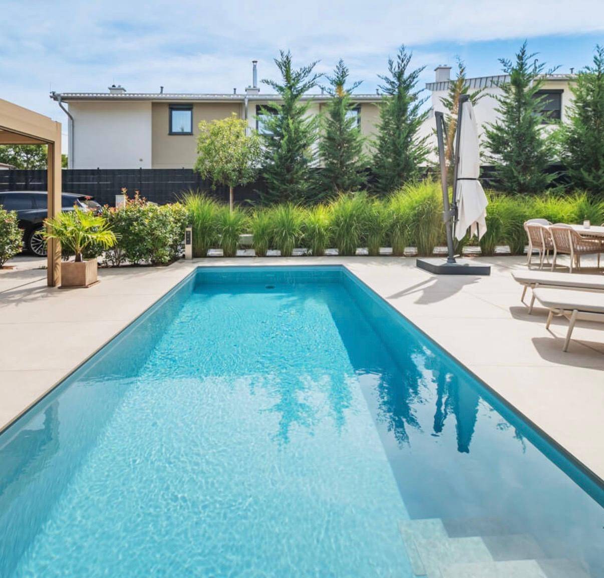 Langer, rechteckiger Pool im Gartenbereich, umgeben von einer gepflegten Terrasse und grünen Pflanzen.