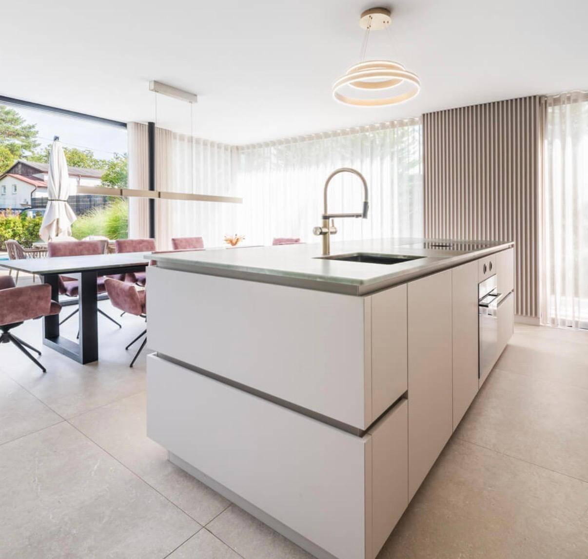 Moderne Küche mit Kochinsel und Essbereich, durch große Fenster zum Garten und Pool hin offen.