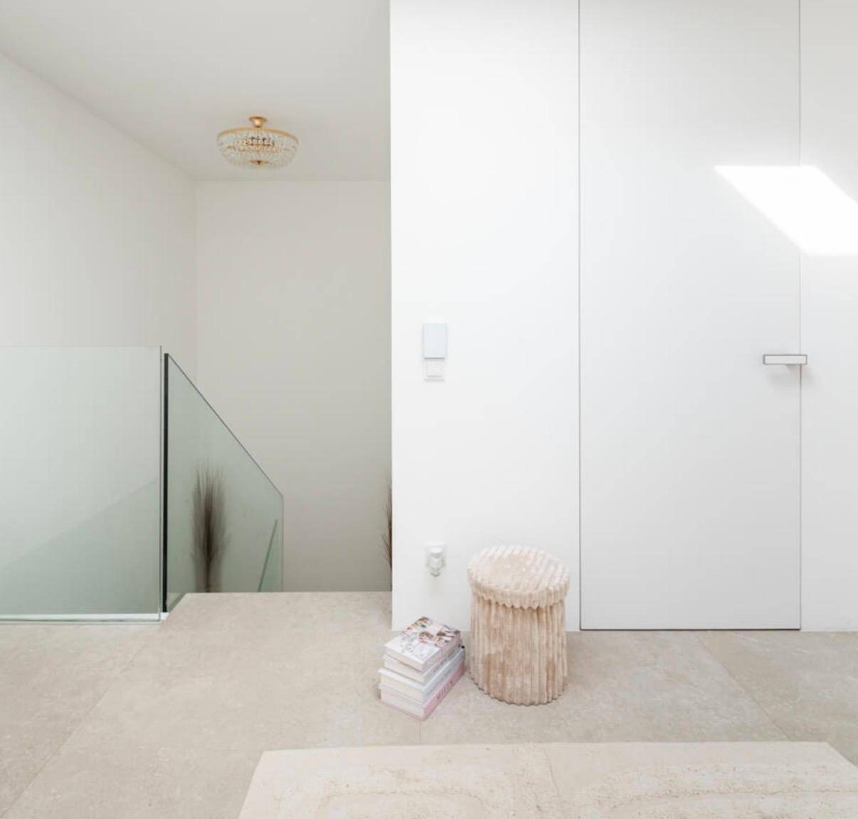 Heller Flurbereich mit minimalistischem Design, Glasgeländer und einem dekorativen Hocker.