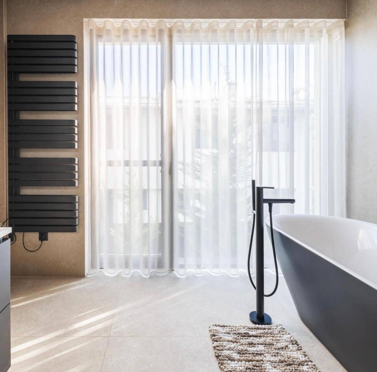 Elegantes Badezimmer mit freistehender Badewanne, großem Fenster und beheiztem Handtuchhalter.