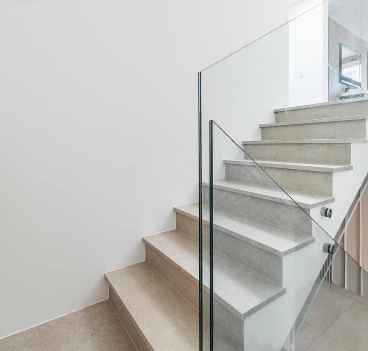 Moderne Treppe mit Glasgeländer und hellen Stufen, die die verschiedenen Ebenen verbindet.
