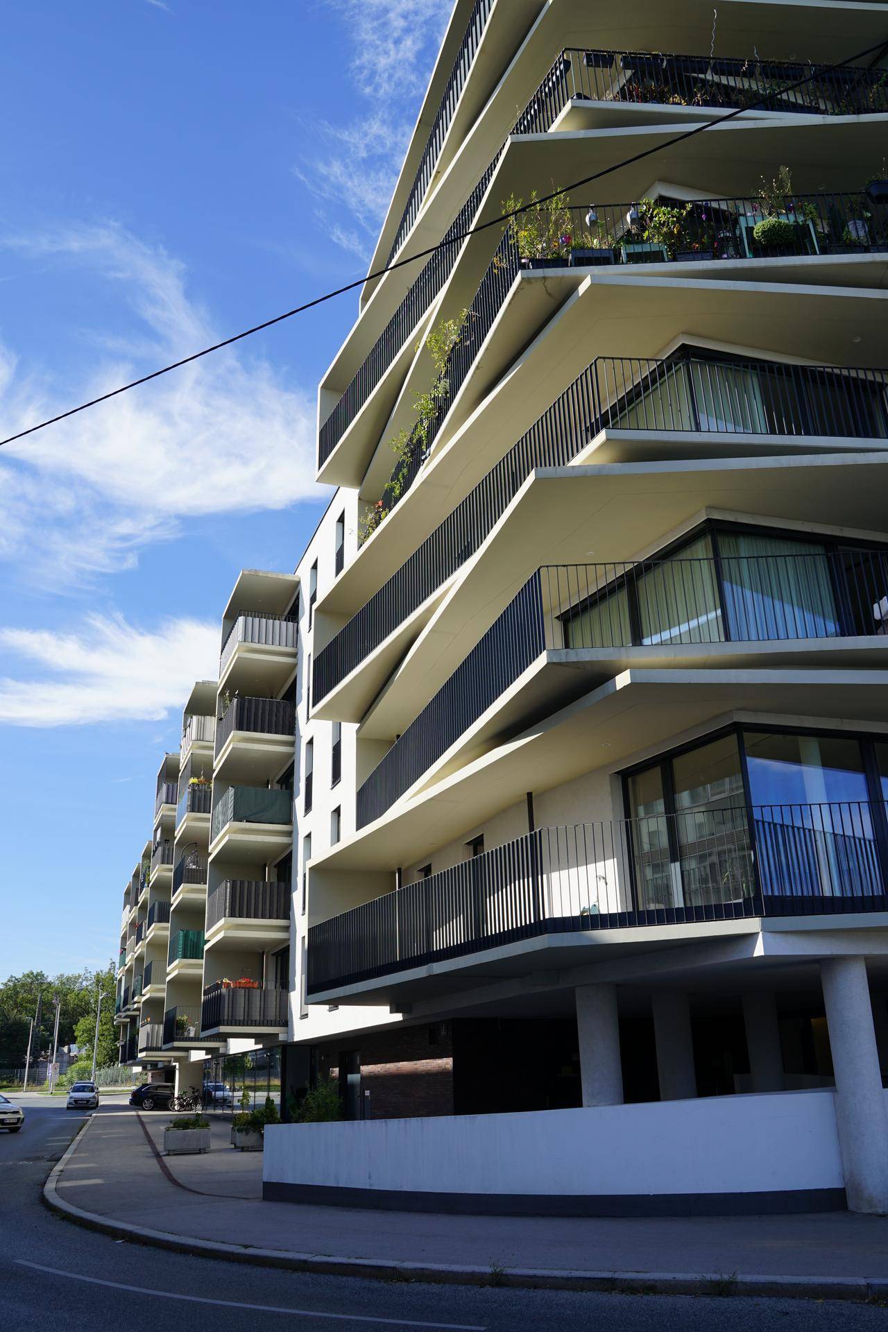 Moderne Architektur eines Wohngebäudes mit gestuften Balkonen und großen Fensterfronten an einer Straße.