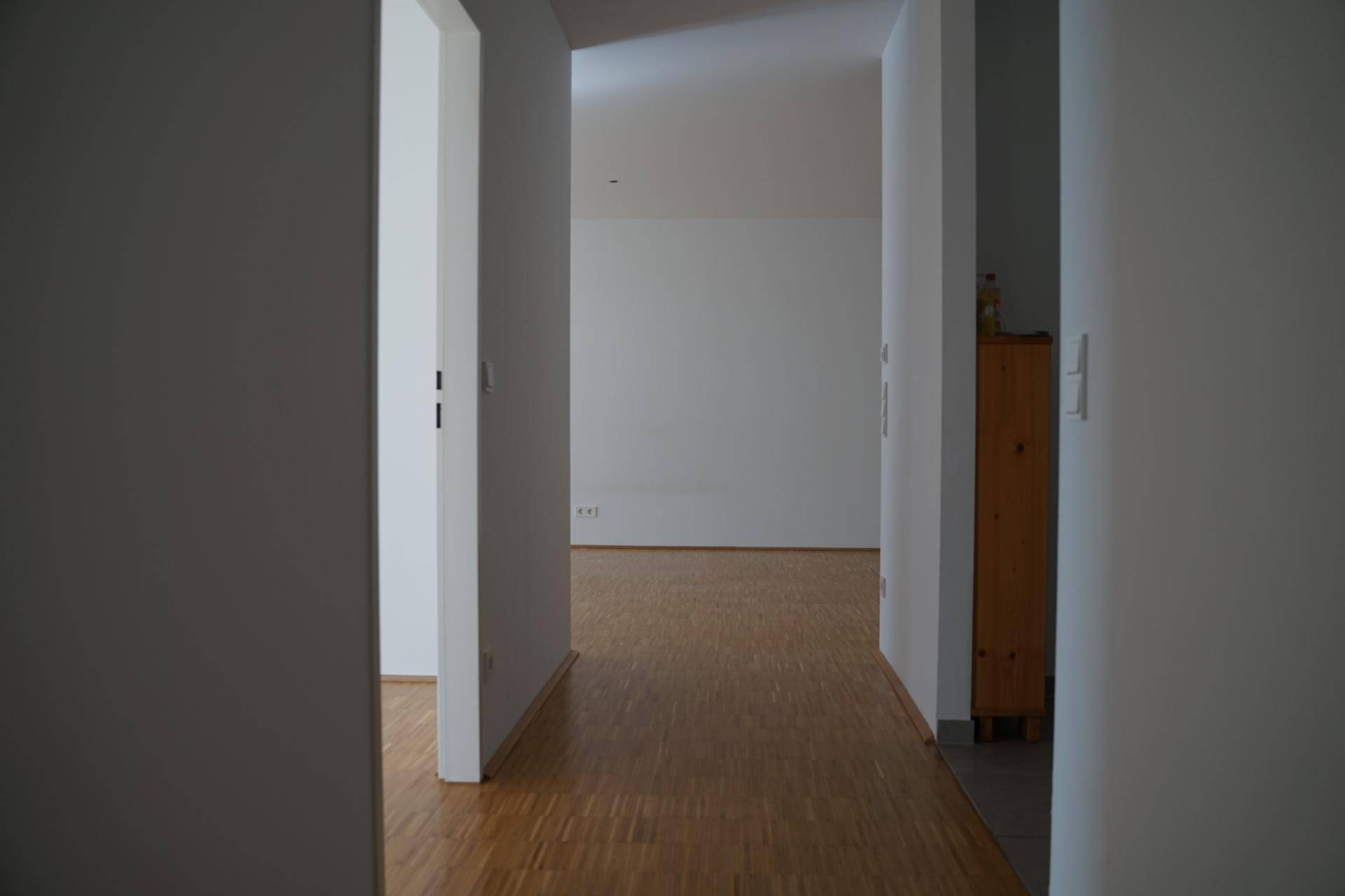 Heller Flur mit Holzparkett, der den Blick in einen weiteren leeren Raum der Wohnung freigibt.
