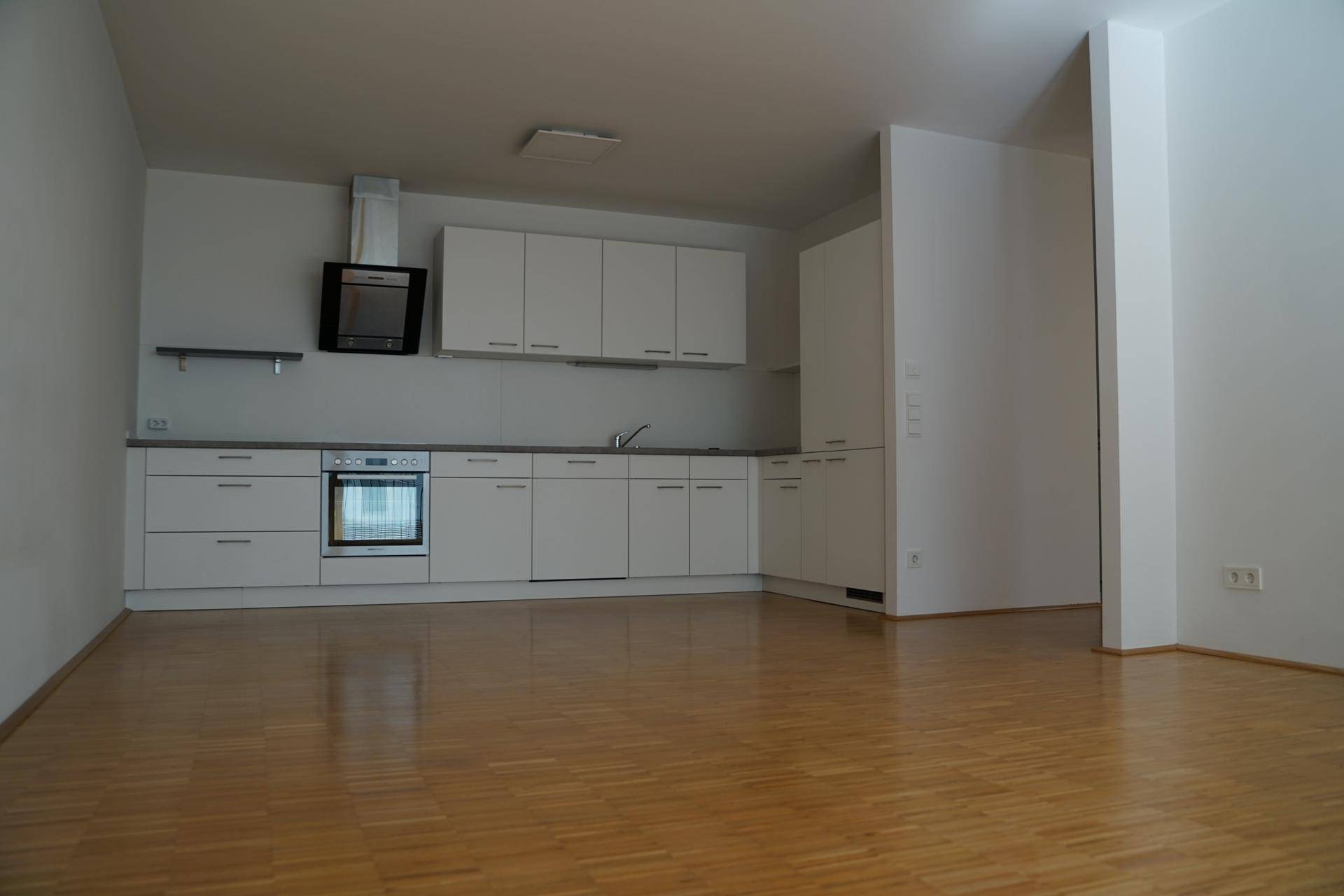 Offene Küche mit weißen Einbauschränken und Holzparkett, bereit zur individuellen Gestaltung des Raumes.