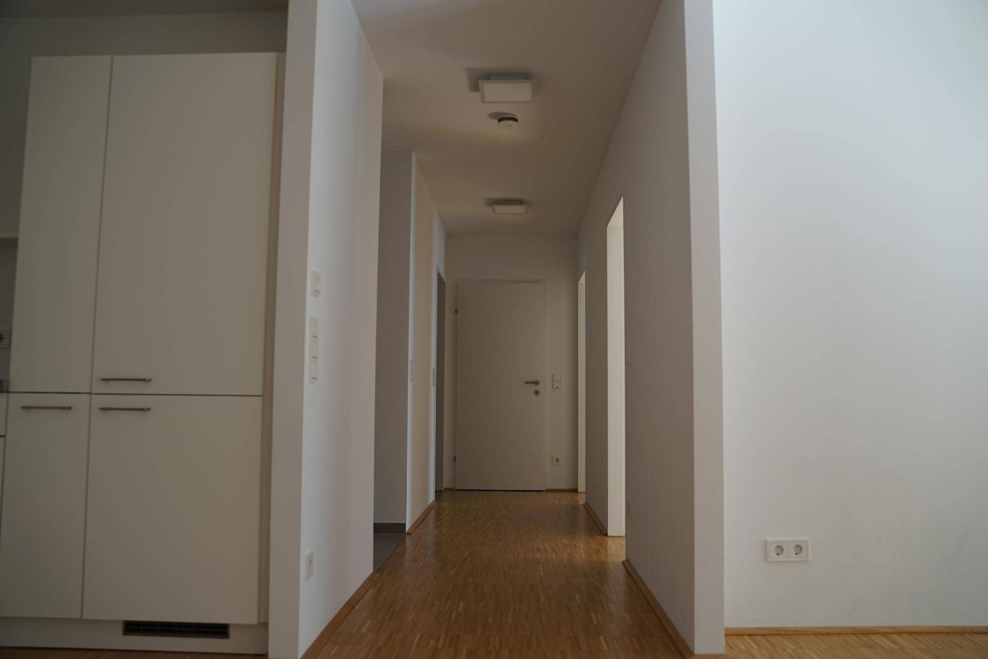 Langer, heller Flur mit Holzparkett und weißen Wänden, der zu weiteren Räumen der Wohnung führt.
