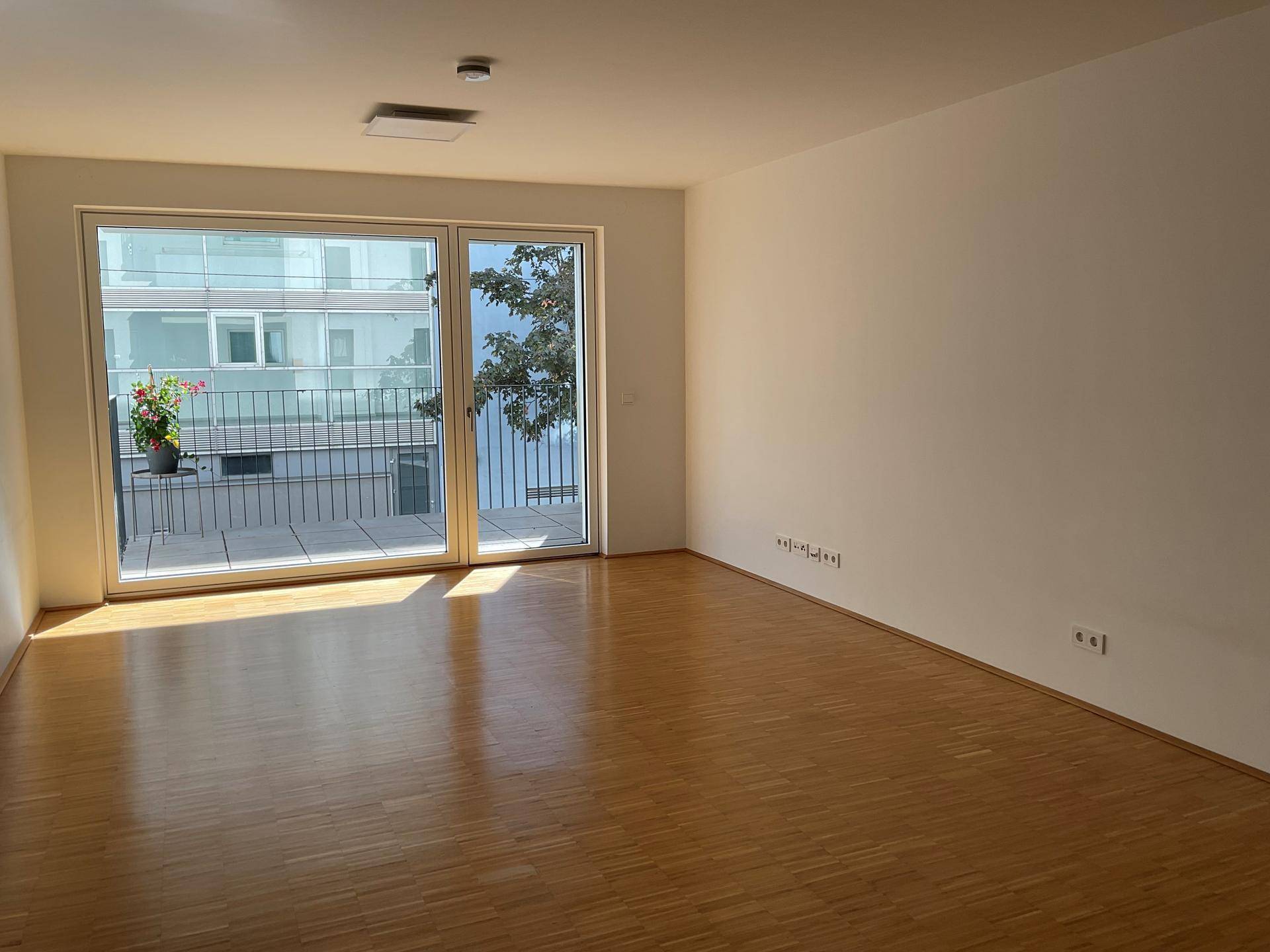 Helles Wohnzimmer mit Parkettboden und Zugang zu einem sonnigen Balkon, ideal für Entspannung.