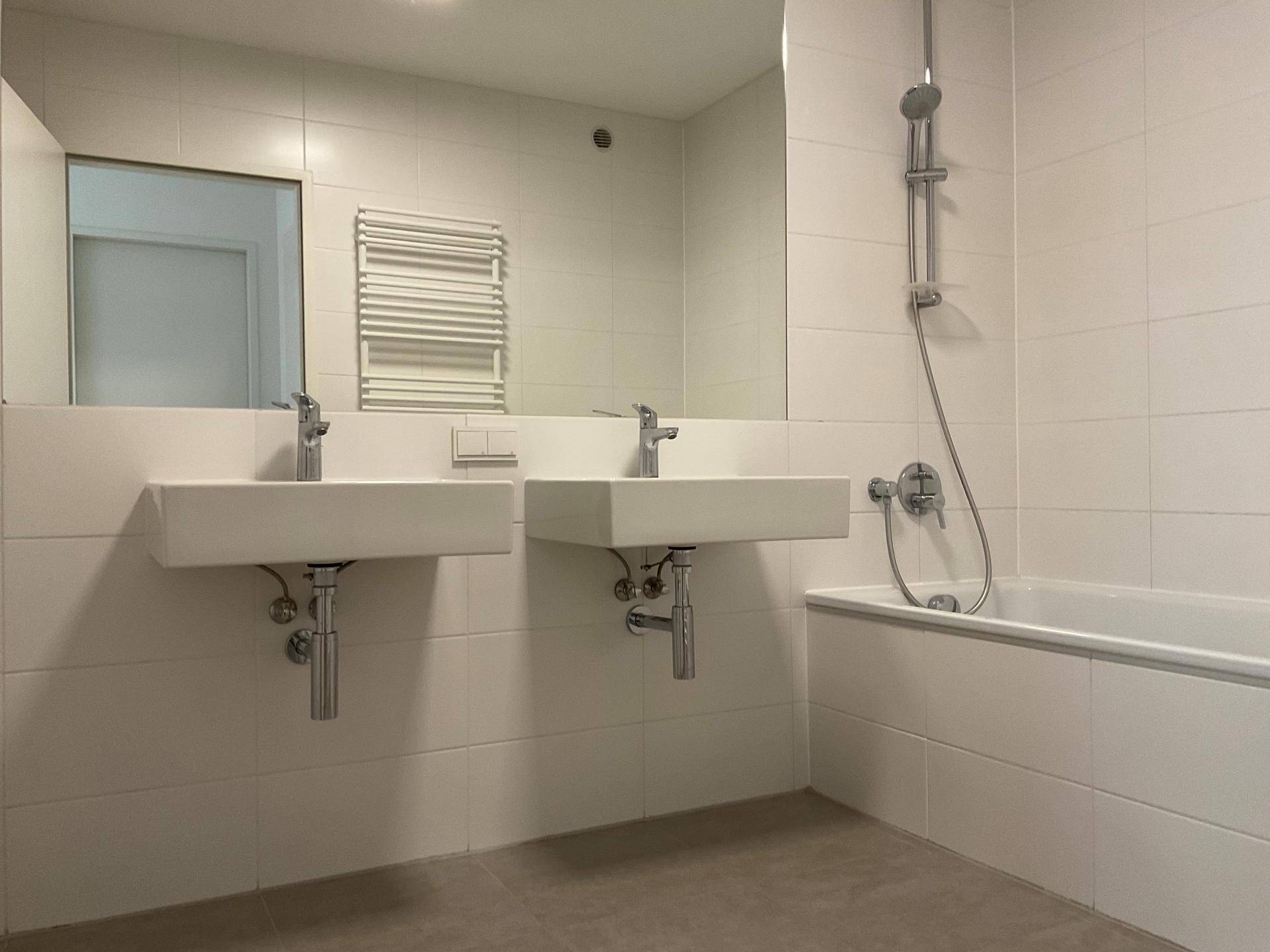 Modernes Badezimmer mit Doppelwaschbecken, Badewanne und weiß gefliesten Wänden, sehr gepflegt.