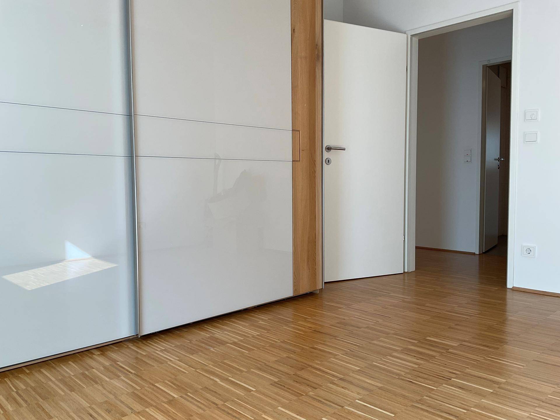 Schlafzimmer mit großem Einbauschrank und Holzparkett, bietet viel Stauraum und Helligkeit.