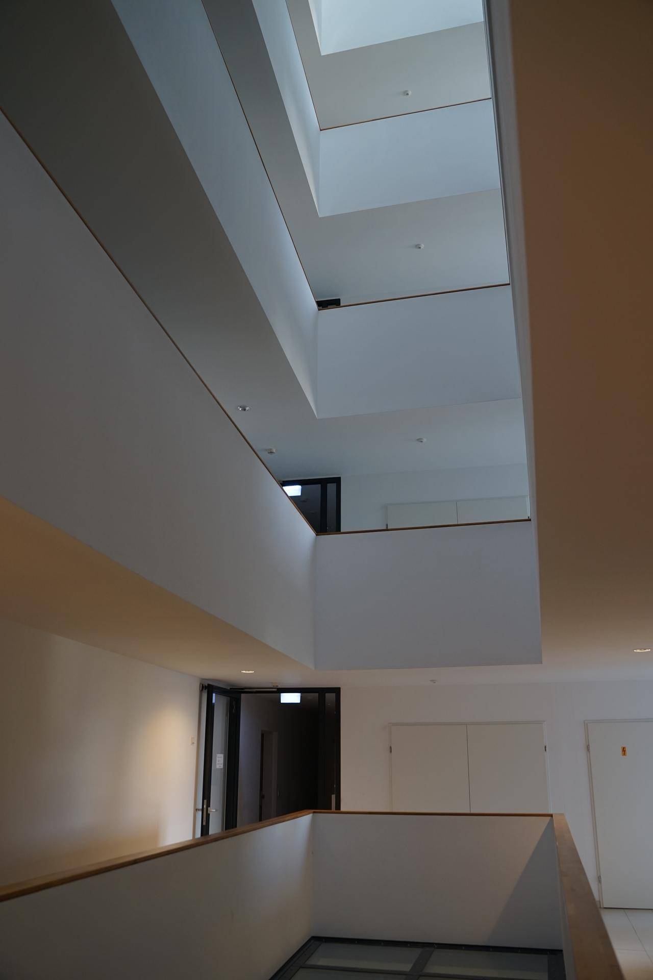 Heller, moderner Treppenaufgang mit mehreren Ebenen und viel Tageslicht von oben durch ein Oberlicht.